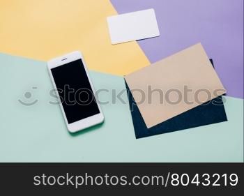 Creative flat lay style workspace desk with smartphone and blank envelope and name card on modern colorful background