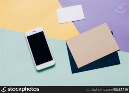 Creative flat lay style workspace desk with smartphone and blank envelope and name card on modern colorful background