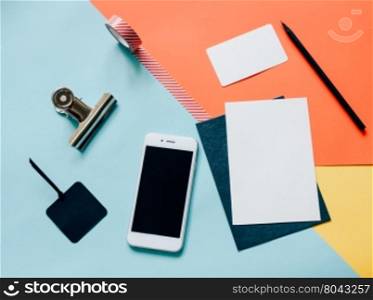 Creative flat lay style workspace desk with smartphone, blank envelope, tag and masking tape on modern colorful background