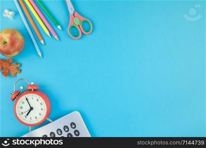 Creative flat lay top view back to school concept with alarm clock, color school and office supplies on bright turquoise paper table frame background with copy space, template for text or design