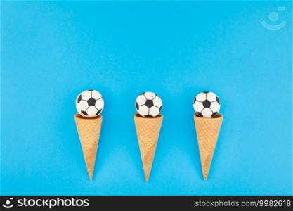Creative flat lay top view of ice cream waffle cones with soccer balls macarons on bright bold blue background with copy space in minimal style, concept of football games for children birthday