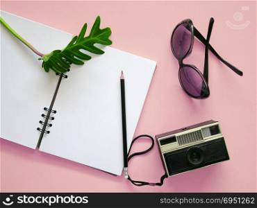 Creative Flat lay travel accessories with notebook ,camera and sunglasses on pink background.