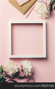 Creative flat lay with flowers, notebook, glasses, mobile phone and white wooden frame on pink background. Feminine fashion