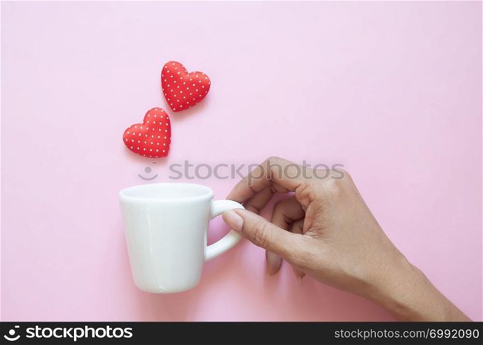 Creative flat lay, woman hand holding white cup with polka dots red hearts on pink background.