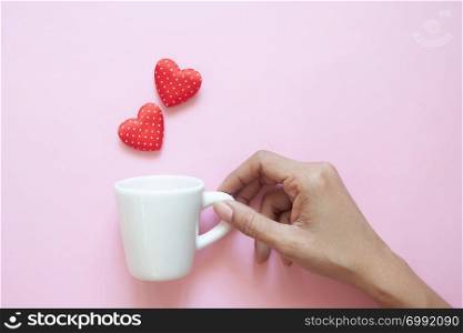 Creative flat lay, woman hand holding white cup with polka dots red hearts on pink background.