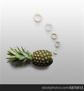 Creative food concept of a fish made of a delicious ripe pineapple, making bubbles with onion rings on grey background.