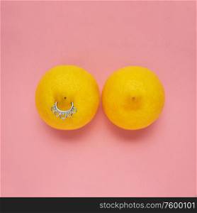 Creative food health fashion concept photo of lemons in shape of woman breast with nipple piercing on pink background.