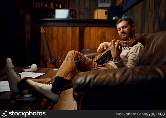Creative guitar player sitting on couch practicing at home. Music education, skills improvement. Guitar player practicing on couch at home