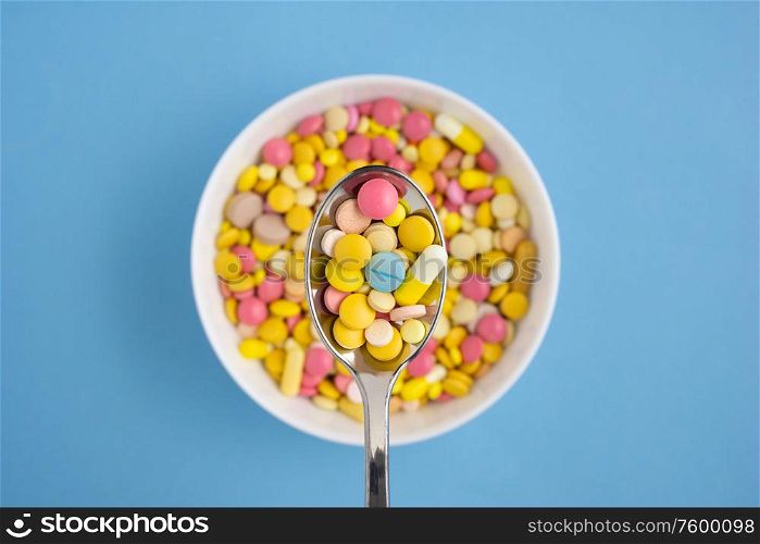 Creative health diet medicine concept photo of pills and drugs in plate with spoon on blue background.. What do you eat.