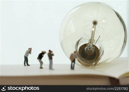 Creative idea concept - miniature photographer with vintage light bulb on open paper notebook
