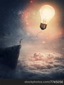 Creative idea concept with a person on the edge of a cliff holding the string of a lightbulb kite or a bulb balloon. Surreal adventure, conceptual scene, genius thinking