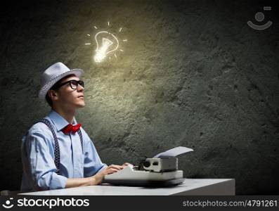 Creative inspiration. Young funny man in glasses writing on typewriter