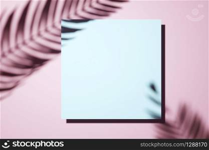 Creative layout made of Shadow of a palm frond on a pink pastell wall with central blank square canvas or picture frame in an interior design template concept. Border arrangement