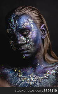 Creative makeup girl with rhinestones and feathers on a dark background. Fantasy face art makeup girl