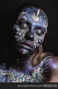 Creative makeup girl with rhinestones and feathers on a dark background. Fantasy face art makeup girl