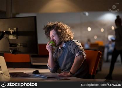 creative man is working in his night office and eating apple
