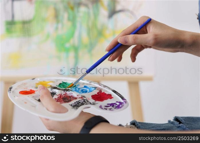 Creative of art concept, Hand of young asian woman hold paintbrush to dip in palette for painting.