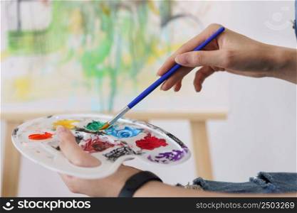 Creative of art concept, Hand of young asian woman hold paintbrush to dip in palette for painting.