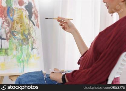 Creative of art concept, Young asian woman sit in studio and hold paintbrush to pointing on artwork.