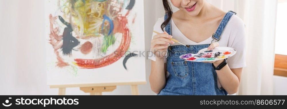 Creative of art concept, Young asian woman use paintbrush to dip in palette for painting on canvas.