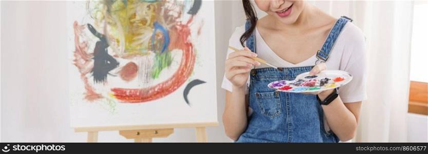 Creative of art concept, Young asian woman use paintbrush to dip in palette for painting on canvas.