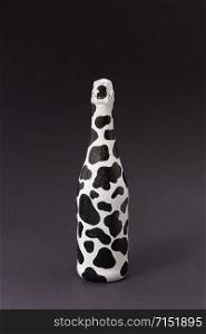 Creative painted wine bottle white with dark spots on a black background, copy space. Minimalism concept.. Holiday painted wine bottle with black spots on a dark gray.