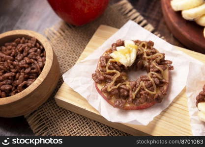 Creative party snack for holidays. Apple rounds with peanut butter, caramel and chocolate flavor puffed rice topping with banana slices. Funny appetizer for kids and adults.