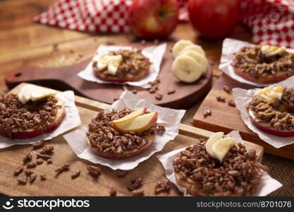 Creative party snack for holidays. Apple rounds with peanut butter, caramel and chocolate flavor puffed rice topping with banana slices. Funny appetizer for kids and adults.