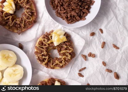 Creative party snack for holidays. Apple rounds with peanut butter, caramel and chocolate flavor puffed rice topping with banana slices. Funny appetizer for kids and adults.