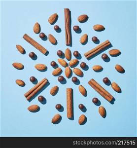 Creative pattern, composition with almonds, cinnamon sticks and chocolate balls on a blue paper background with hard shadows. Top view.. Symmetrical circular pattern from a almonds nuts, cinnamon and chocolate balls on a blue background. Flat lay