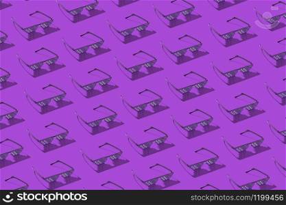 Creative pattern from protective pixel glasses using for work with computer screens, phones and TV on a purple background with hard shadows.. Diagonal pattern from computer pixel glasses.