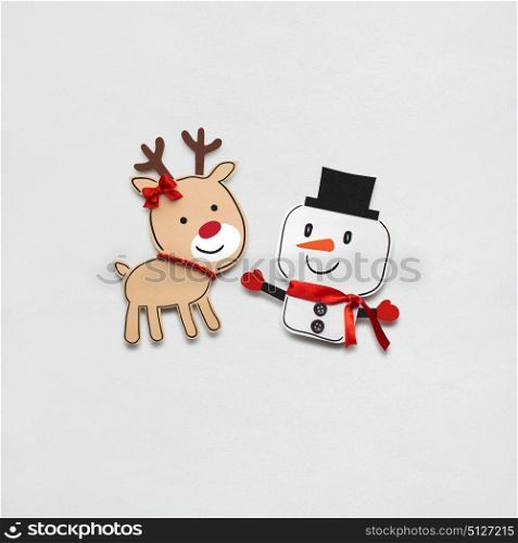 Creative photo of a snowman and a deer made of paper on grey background.