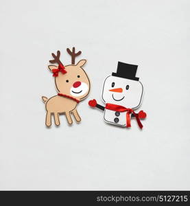 Creative photo of a snowman and a deer made of paper on grey background.