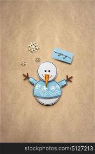 Creative photo of a snowman made of paper on brown background.