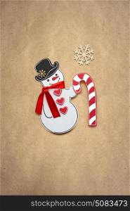 Creative photo of a snowman with a candy made of paper on brown background.