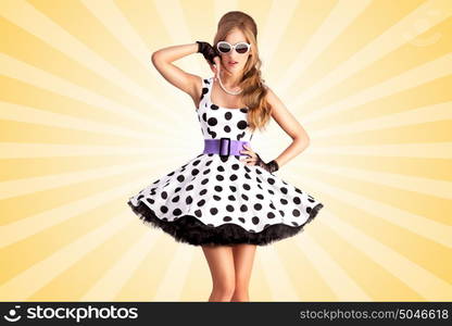 Creative photo of a vogue pin-up girl, dressed in a retro polka-dot dress and sunglasses, posing on colorful abstract cartoon style background.