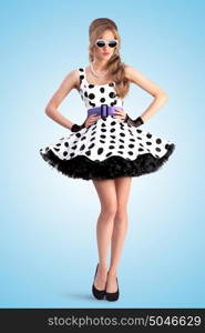 Creative photo of a vogue pin-up girl, dressed in a retro polka-dot dress and sunglasses, posing on blue background.