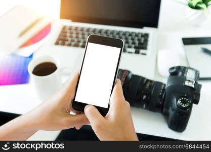 creative photogeapher holding phone white screen on workspace table, phone blank screen for adjustment mobile app