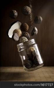 creative photography composition of delicious flying chocolate truffles and floating glass jar on wooden background