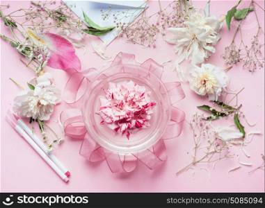 Creative Pink Florist workspace. Pretty floral decoration arrangement with pink roses and plant leaves in glass vase with water and florist decoration equipment, top view. Holiday concept