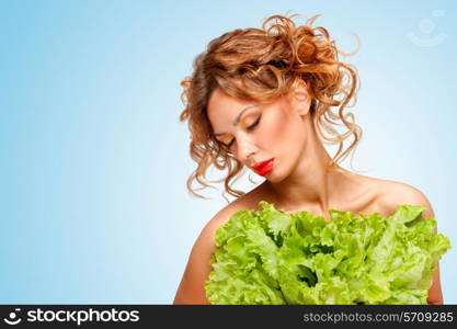 Creative portrait of a beautiful topless girl on a diet hiding behind green leaves of lettuce, that look like an eco-green dress on blue background.