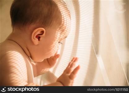 Creative portrait of a child with a pattern of lights and shadows on his face created to pass sunlight through a net at balcony. Shallow depth of field.
