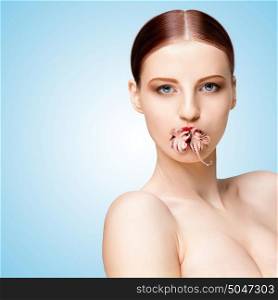 Creative portrait of a nude girl with beautiful face and body holding cooked baby octopus in mouth on blue background.