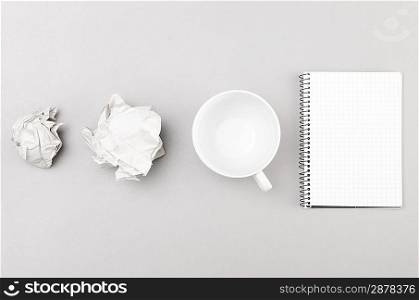 creative process. crumpled wads, notebook and cup on gray