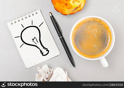 creative process. crumpled wads, notebook with bulb picture and cup