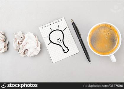 creative process. crumpled wads, notebook with bulb picture and cup
