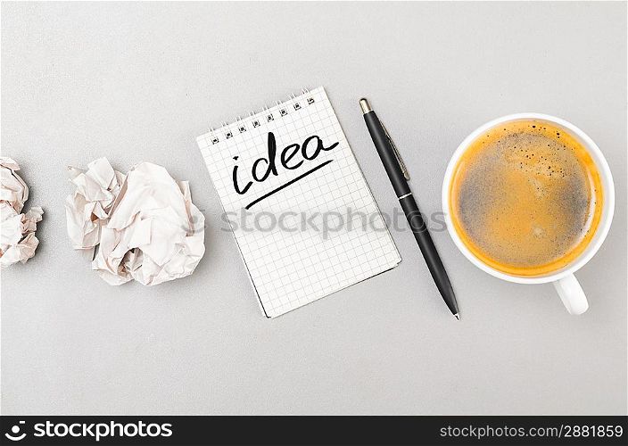 creative process. crumpled wads, notebook with idea word and cup