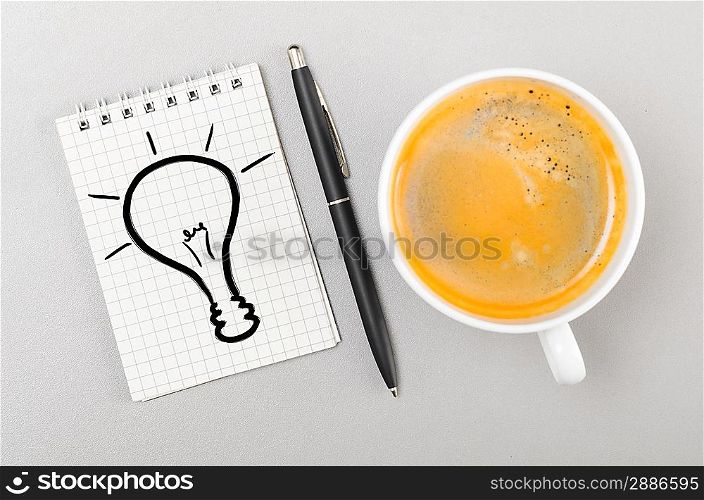 creative process. notebook with bulb picture and cup on gray