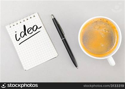 creative process. notebook with idea word and cup on gray