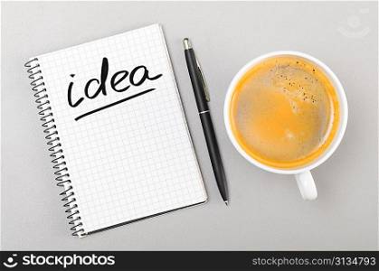 creative process. notebook with idea word and cup on gray